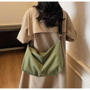 Detail view of green plaid tote bag with adjustable black strap on a khaki trench coat