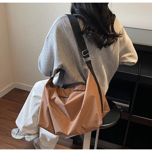 Detailed view of brown plaid tote bag with wide black strap and silver buckle on model
