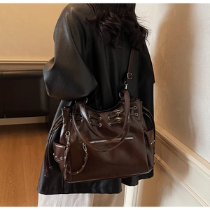 Détail du cabas marron foncé avec œillets métalliques et texture cuir brillant