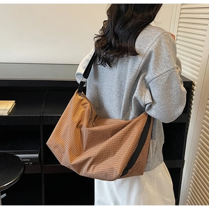 Brown checkered tote bag with wide black strap shown on shoulder in a minimalist setting