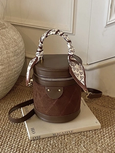 Dark brown leather bucket bag with quilted patterns and silk scarf handle on a magazine