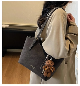 Detail of dark grey suede tote bag with white stitching and plush bear pendant