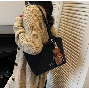 Detail of black tote bag with white stitching and cute brown teddy bear keychain accessory