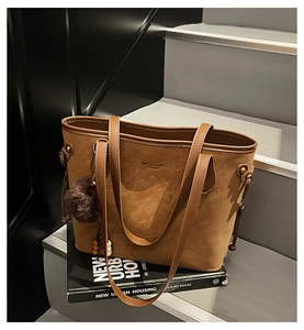 Detail of tan suede-like tote bag featuring side drawstrings and a fuzzy pom-pom charm