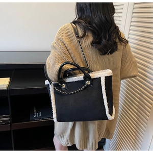 Close-up of black tote bag with white faux fur trim and gold chain detail on model