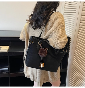 Detail of black leather tote bag with gold hardware and plush charm on a shoulder