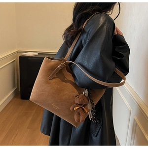 Detail of vintage brown suede tote bag with plush bear charm and striped silk scarf