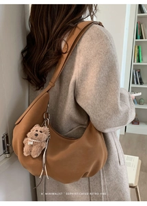 Sac hobo en daim marron avec breloque peluche porté par un mannequin en intérieur