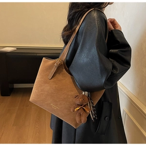 Brown suede tote bag with plush bear charm worn on a black leather jacket by a model