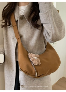 Détail du sac bandoulière croissant en daim caramel avec charm ours et texture plissée