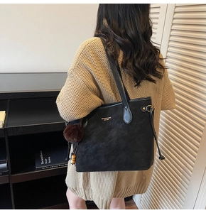 Close-up of a black matte tote bag with golden lettering and a brown fur charm