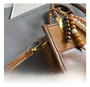 Detailed close-up of brown patchwork leather bag with woven handle and wooden bead tassel