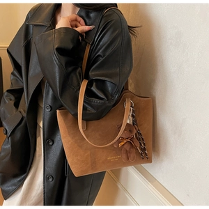 Detail of a large brown suede tote bag with a golden logo and a cute plush bear charm