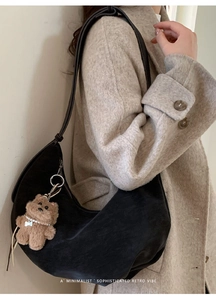 Détail du sac hobo en daim noir avec breloque ours en peluche sur fond manteau beige