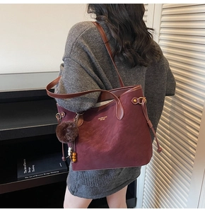 Detail of burgundy faux suede tote bag featuring pom-pom charm and gold lettering