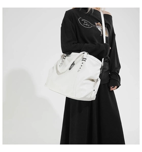 Detail of white leather tote bag with star studs and side zipper shown on model
