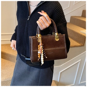 Detail of dark brown leather crossbody bag with braided handle and colorful bead charm
