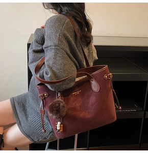 Burgundy tote bag detail showing matte texture with plush pompom and side drawstring