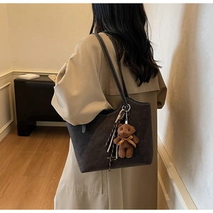 Detail of dark brown tote bag with white stitching and plush bear charm on a model