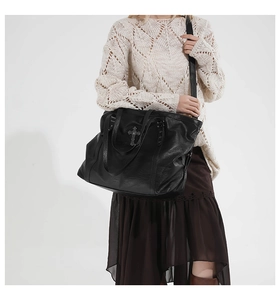 Side view of black leather tote bag with vintage metal cross detail on a female model