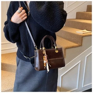 Detail of deep brown crossbody bag with woven handle and beaded charm accessory