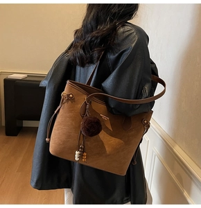 Close-up of brown suede tote bag featuring plush pom-pom and wooden bead tassel details