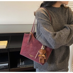 Close-up of burgundy leather tote bag with gold lettering and a cute brown bear charm