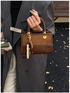 Detail of brown patchwork tote bag featuring a woven handle and beaded charm accessory