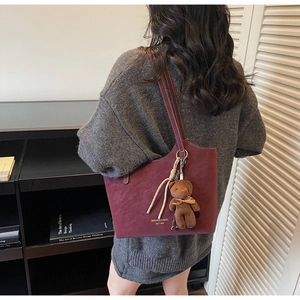 Detail of burgundy leather tote bag with cute plush bear and woven cord charms