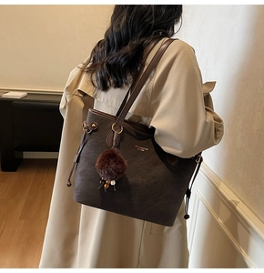 Detail of dark brown tote bag with plush ball charm and brand logo for commuting