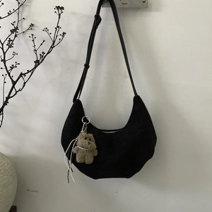 Détail d'un sac demi-lune en daim noir avec un charmant pendentif de chiot en peluche