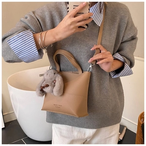 Brown faux leather tote bag with plush rabbit charm and shoulder strap on grey sweater