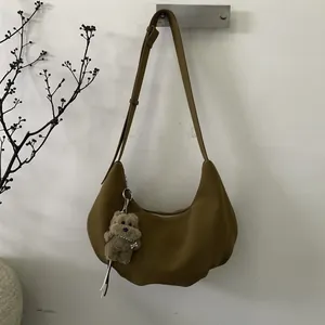 Détail d'un sac demi-lune kaki foncé avec un charmant pendentif chien en peluche sur la bandoulière