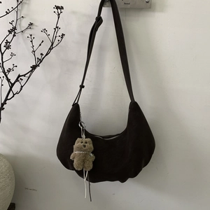 Détail du sac demi-lune en daim marron foncé avec bandoulière réglable et pendentif ours