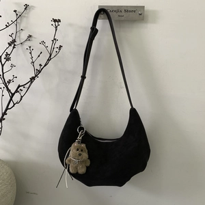 Détail du sac croissant en daim noir avec un charm ours en peluche et bandoulière réglable