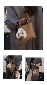 Detailed shot of brown textured leather bucket bag with a cute white rabbit plush charm