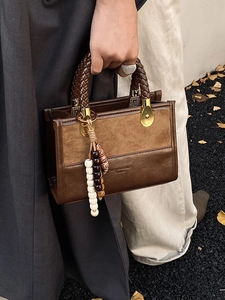 Brown leopard-style crossbody bag with woven handle and beaded charm accessory