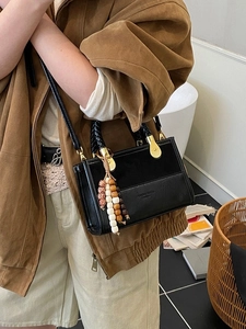Black PU leather handbag with woven handle and bead pendant shown in warm indoor setting