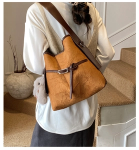 Detail of ginger leather bucket bag with brown strap and plush bunny charm on a model