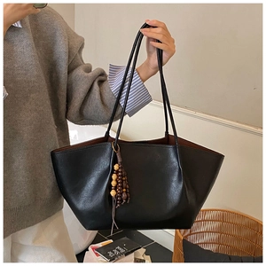 Detail of black wax leather tote bag with wooden bead tassel and long handles for women