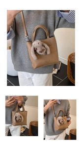 Detail of beige tote bag with a grey plush rabbit charm and detachable shoulder strap