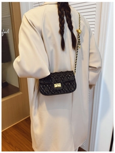 Detailed back view of a black quilted shoulder bag with gold chain strap on a model