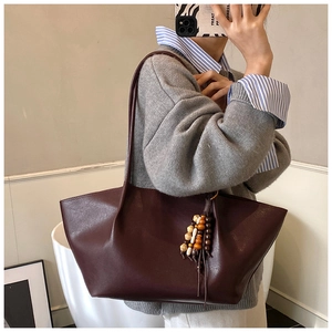 Close-up of wine red leather tote bag with boho wooden bead tassels and matte texture