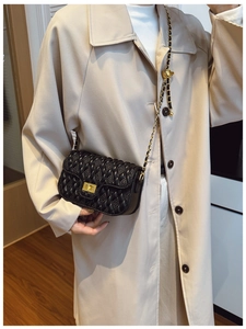 Detail of a black quilted leather crossbody bag with gold hardware and chain strap