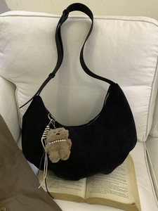 Sac hobo noir en daim avec charm d'ours en peluche marron sur un canapé blanc