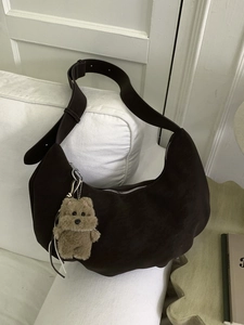 Grand sac hobo en daim marron foncé avec pendentif ours en peluche sur un canapé blanc