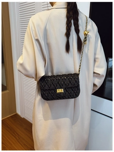 Detail of a black quilted shoulder bag with gold twist lock on a beige coat