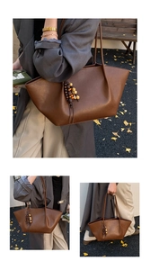 Detail of vintage brown tote bag with beaded tassel charm and smooth leather texture