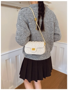 Back view of a white quilted crossbody bag with gold chain strap worn by a model