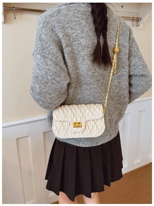 Rear view of model wearing white quilted crossbody bag with gold chain and turn-lock
